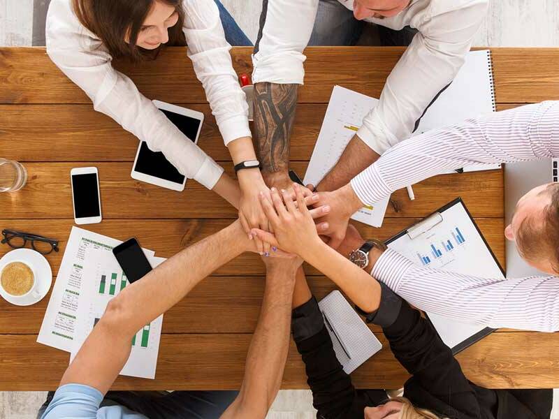 professionals at a meeting table with everybody's hands on top of each other