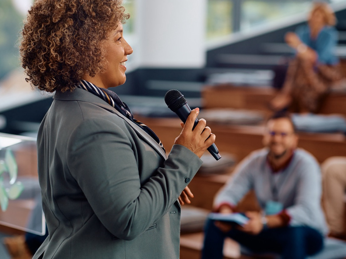 Happy businesswoman giving a speech to group of people during a seminar in conference hall.